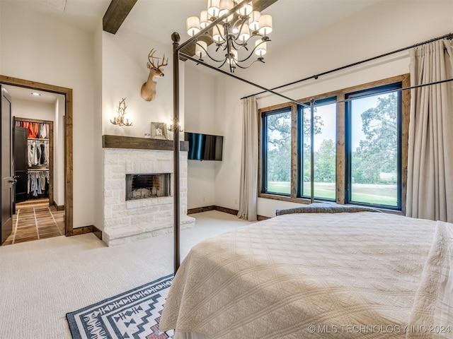 carpeted bedroom with a stone fireplace, a closet, and an inviting chandelier