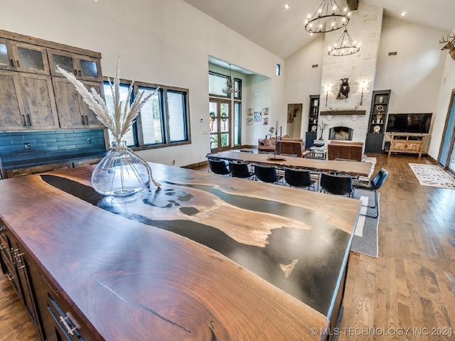 dining area with a stone fireplace, light hardwood / wood-style flooring, high vaulted ceiling, and an inviting chandelier