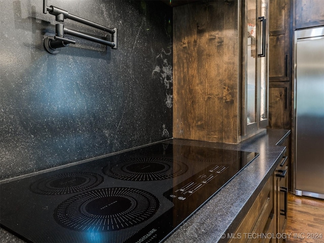 details featuring black electric stovetop, stainless steel refrigerator, and dark wood-type flooring