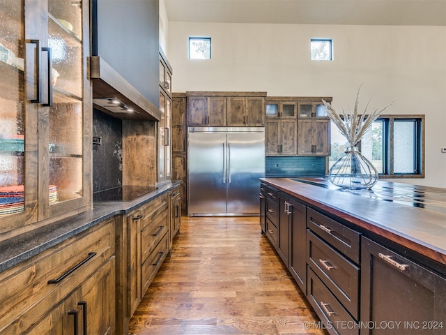 kitchen featuring black electric cooktop, built in fridge, wood-type flooring, and decorative backsplash