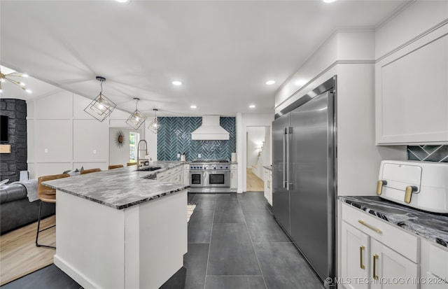 kitchen featuring pendant lighting, sink, white cabinets, high quality appliances, and premium range hood