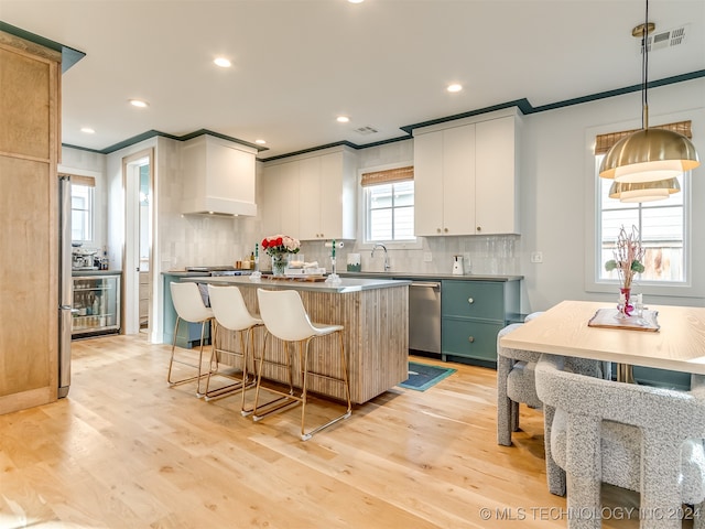 kitchen featuring white cabinetry, dishwasher, pendant lighting, a center island, and light hardwood / wood-style flooring