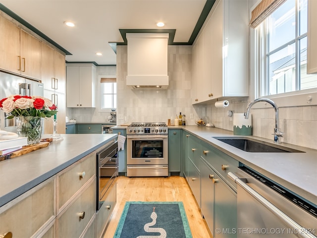 kitchen featuring premium range hood, sink, high end appliances, light hardwood / wood-style flooring, and backsplash