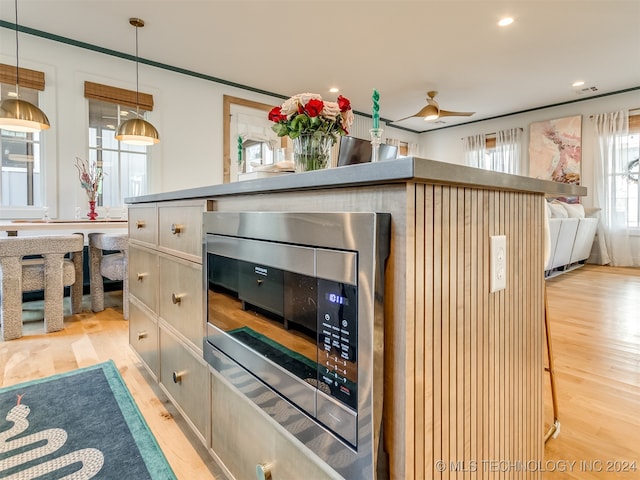 kitchen featuring ceiling fan, stainless steel microwave, light hardwood / wood-style flooring, and hanging light fixtures