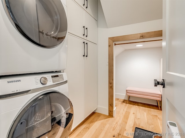 laundry area featuring cabinets, stacked washer / dryer, and light hardwood / wood-style floors