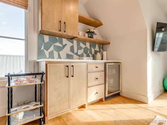 bar featuring light hardwood / wood-style flooring, wine cooler, light brown cabinets, and vaulted ceiling