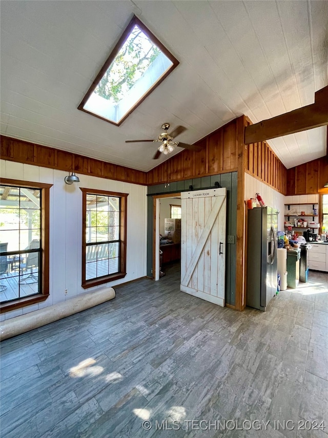 interior space with ceiling fan, vaulted ceiling with skylight, wood walls, and a barn door