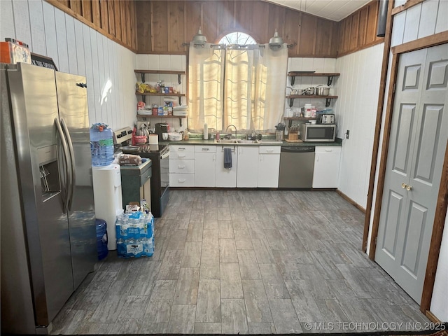 kitchen featuring white cabinets, wooden walls, and appliances with stainless steel finishes