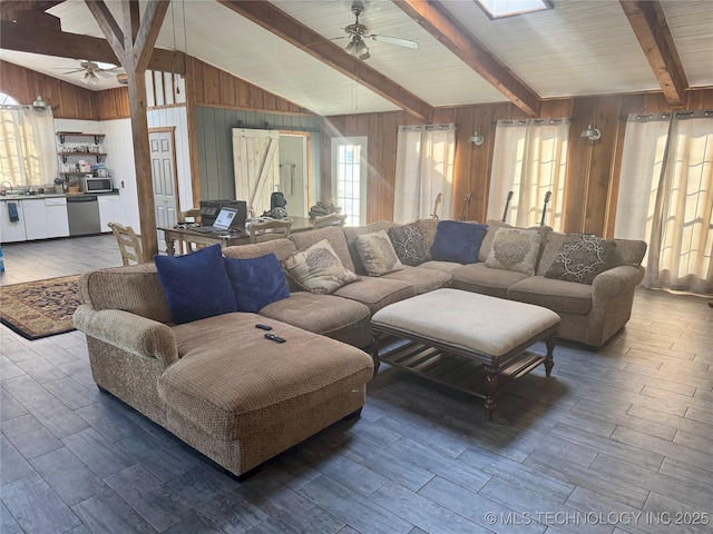 living room featuring ceiling fan, wooden walls, and vaulted ceiling with skylight