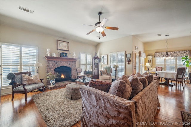 living room with ceiling fan with notable chandelier, a fireplace, dark wood-type flooring, and a wealth of natural light