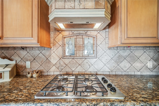 kitchen with stainless steel gas stovetop, dark stone countertops, premium range hood, and tasteful backsplash