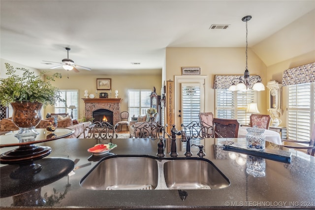 kitchen with hanging light fixtures, ceiling fan with notable chandelier, a fireplace, and a wealth of natural light