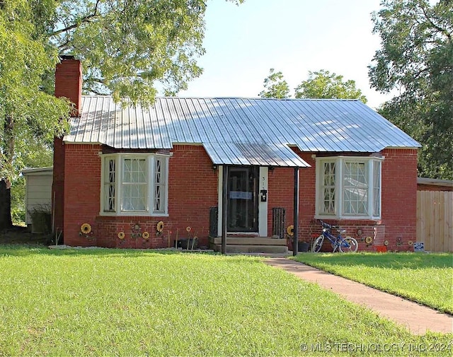 view of front of home with metal roof, brick siding, and a front yard