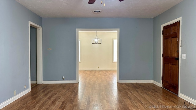 empty room featuring a textured ceiling, wood finished floors, visible vents, a ceiling fan, and baseboards