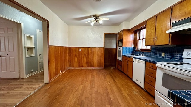 kitchen with light wood finished floors, wainscoting, a sink, wood walls, and white appliances