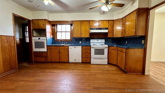 kitchen with white appliances, dark countertops, brown cabinets, and under cabinet range hood