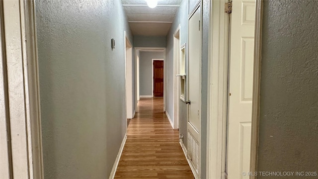 hallway with a textured wall, baseboards, and wood finished floors