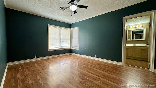 empty room featuring a textured ceiling, ceiling fan, wood finished floors, and baseboards