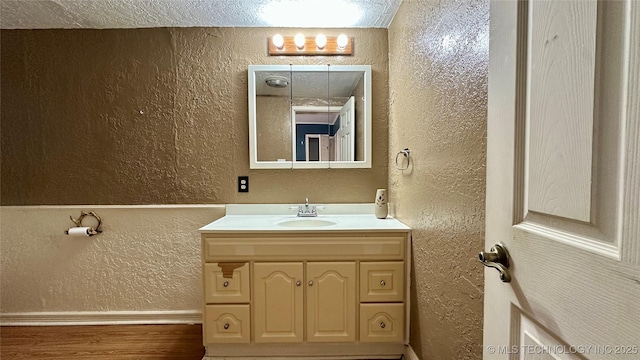 bathroom with a textured wall, vanity, and wood finished floors