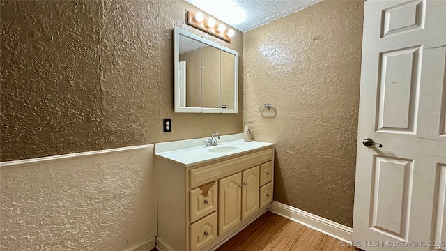 bathroom with a textured wall, wood finished floors, vanity, and baseboards