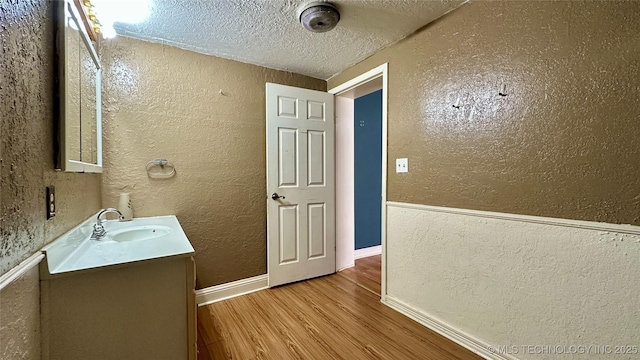 bathroom with baseboards, a textured wall, wood finished floors, a textured ceiling, and vanity