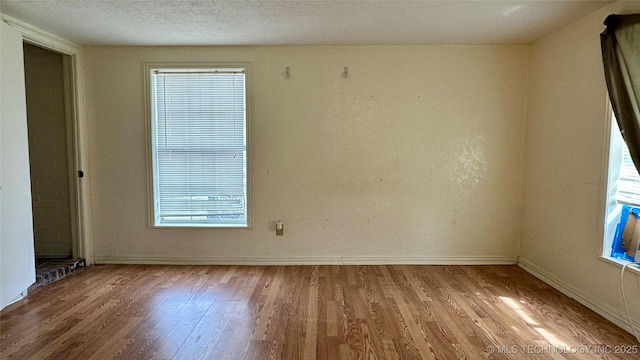 empty room featuring a textured ceiling, wood finished floors, and baseboards