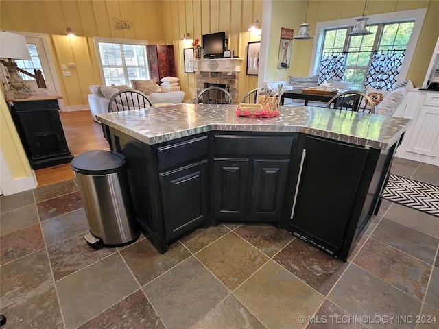 kitchen with a healthy amount of sunlight, a stone fireplace, a kitchen island, and decorative light fixtures