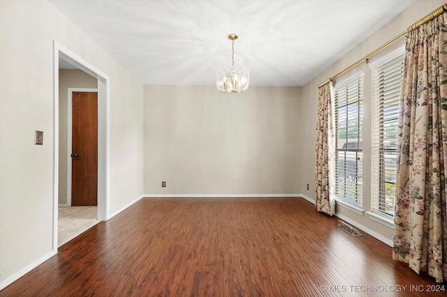 empty room with dark hardwood / wood-style flooring and an inviting chandelier