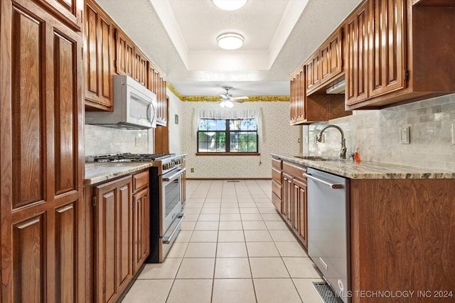 kitchen featuring ceiling fan, sink, a raised ceiling, light tile patterned floors, and appliances with stainless steel finishes