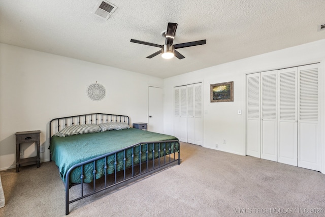 carpeted bedroom featuring two closets, ceiling fan, and a textured ceiling