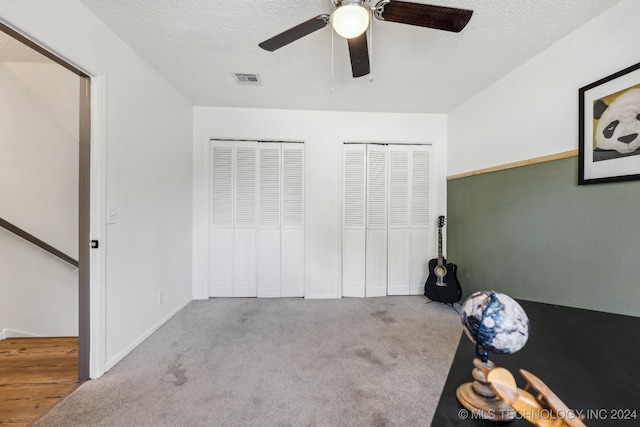 unfurnished bedroom featuring ceiling fan, light colored carpet, a textured ceiling, and two closets