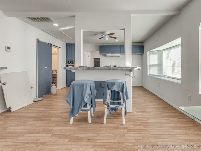 kitchen featuring a breakfast bar, a barn door, kitchen peninsula, blue cabinetry, and light hardwood / wood-style flooring