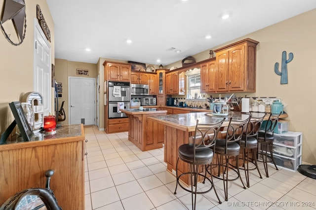 kitchen featuring appliances with stainless steel finishes, a center island, light tile patterned flooring, and a breakfast bar area