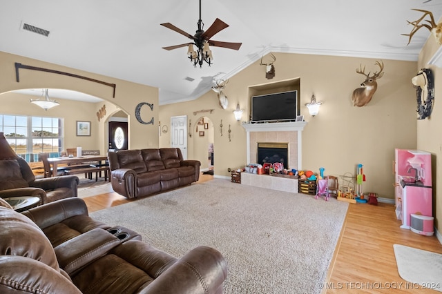 living room featuring ceiling fan, lofted ceiling, light hardwood / wood-style flooring, a tile fireplace, and crown molding