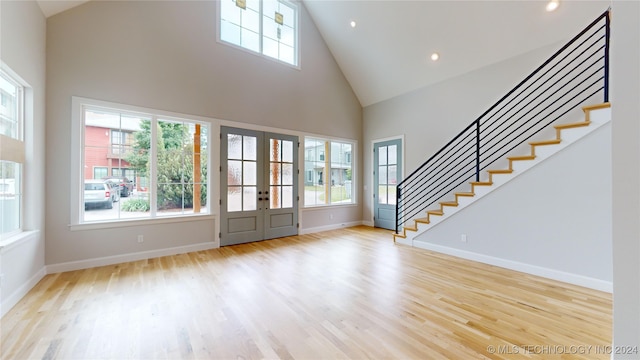 foyer entrance featuring french doors, light wood-type flooring, high vaulted ceiling, and a healthy amount of sunlight