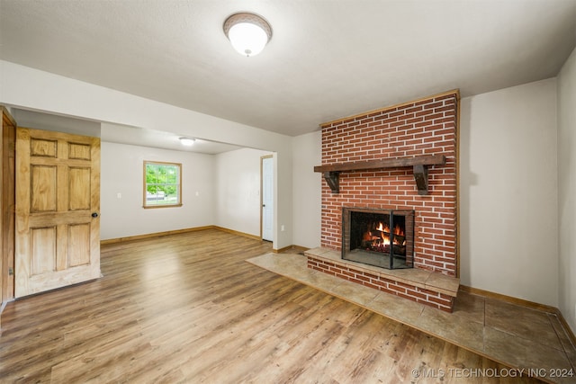 unfurnished living room with wood-type flooring and a brick fireplace