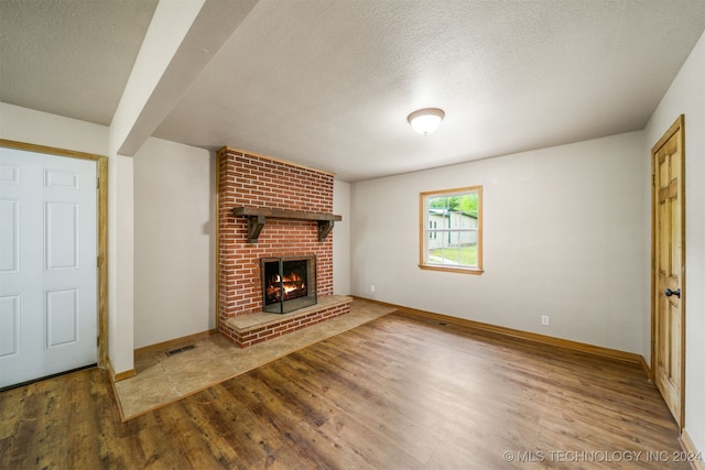 unfurnished living room with a textured ceiling, wood-type flooring, and a brick fireplace