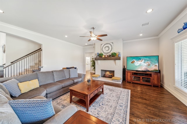 living room featuring a brick fireplace, crown molding, dark wood-type flooring, and ceiling fan