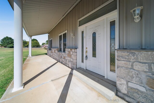 1202 SW 9th St, Wagoner, OK 74467 - doorway to property featuring board and batten siding, a yard, covered porch, and stone siding