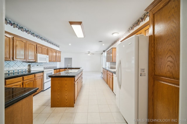 kitchen featuring sink, an island with sink, white appliances, backsplash, and ceiling fan