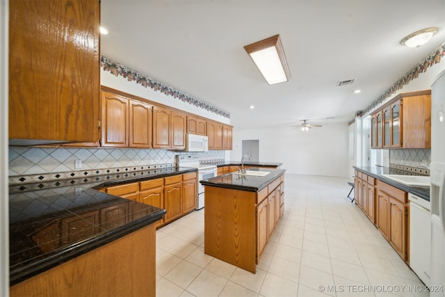 kitchen featuring a center island with sink, backsplash, sink, and white appliances