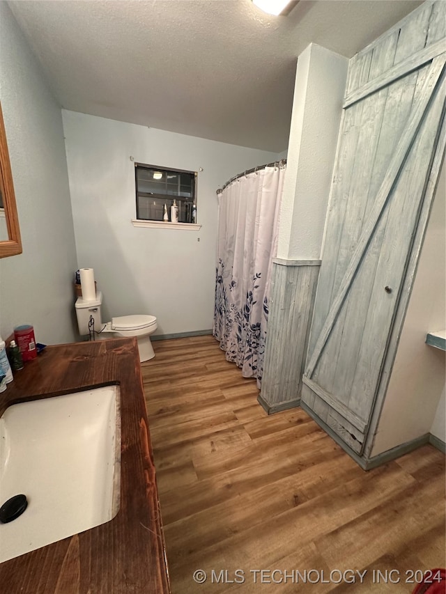 bathroom with toilet, curtained shower, a textured ceiling, hardwood / wood-style flooring, and sink