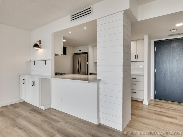 kitchen featuring white cabinets, stainless steel fridge, light hardwood / wood-style floors, and kitchen peninsula