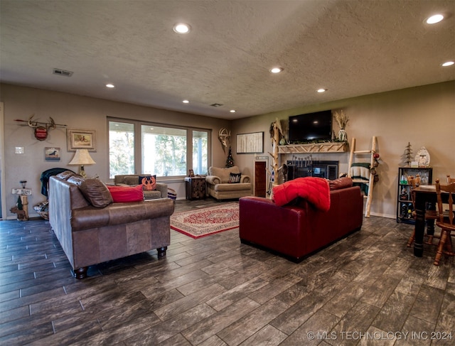 living room with a textured ceiling, a stone fireplace, and dark wood-type flooring