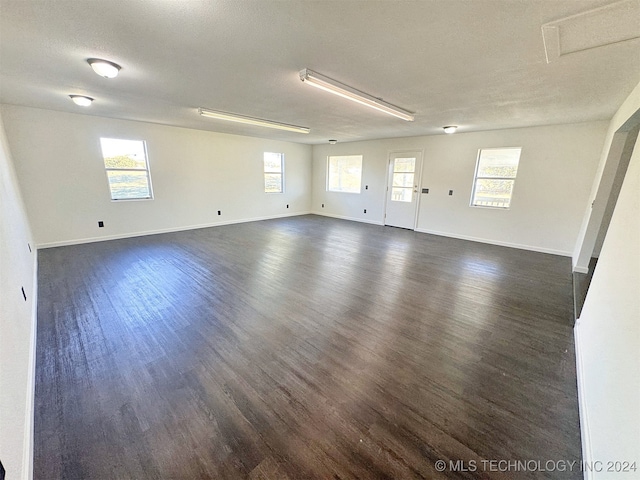 unfurnished room with a textured ceiling, a healthy amount of sunlight, and dark hardwood / wood-style flooring