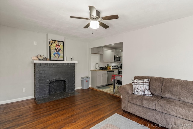 living area with ceiling fan, baseboards, a brick fireplace, and wood finished floors