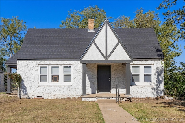 tudor house featuring a front lawn, a chimney, and a shingled roof