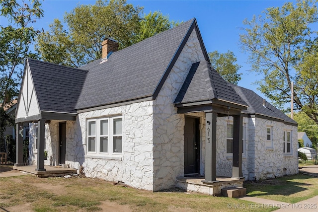 view of front of home with a shingled roof, a front yard, stone siding, and a chimney