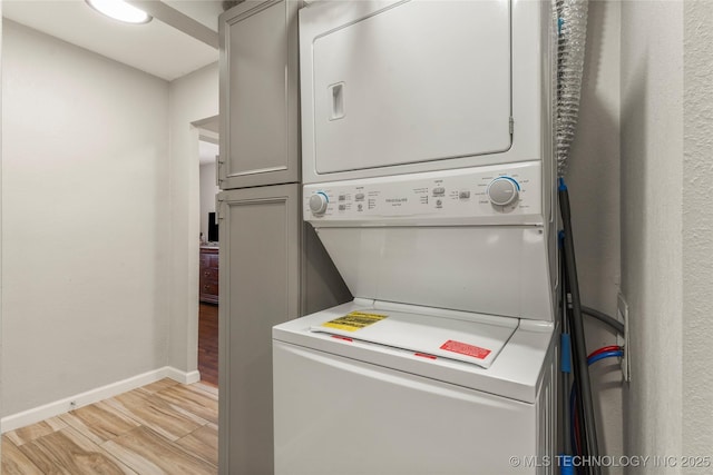 laundry room featuring stacked washer and dryer, cabinet space, baseboards, and light wood finished floors