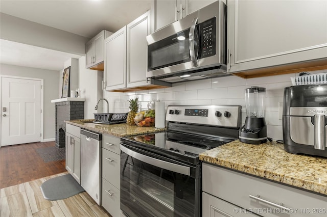 kitchen with light stone counters, decorative backsplash, appliances with stainless steel finishes, wood finished floors, and a sink